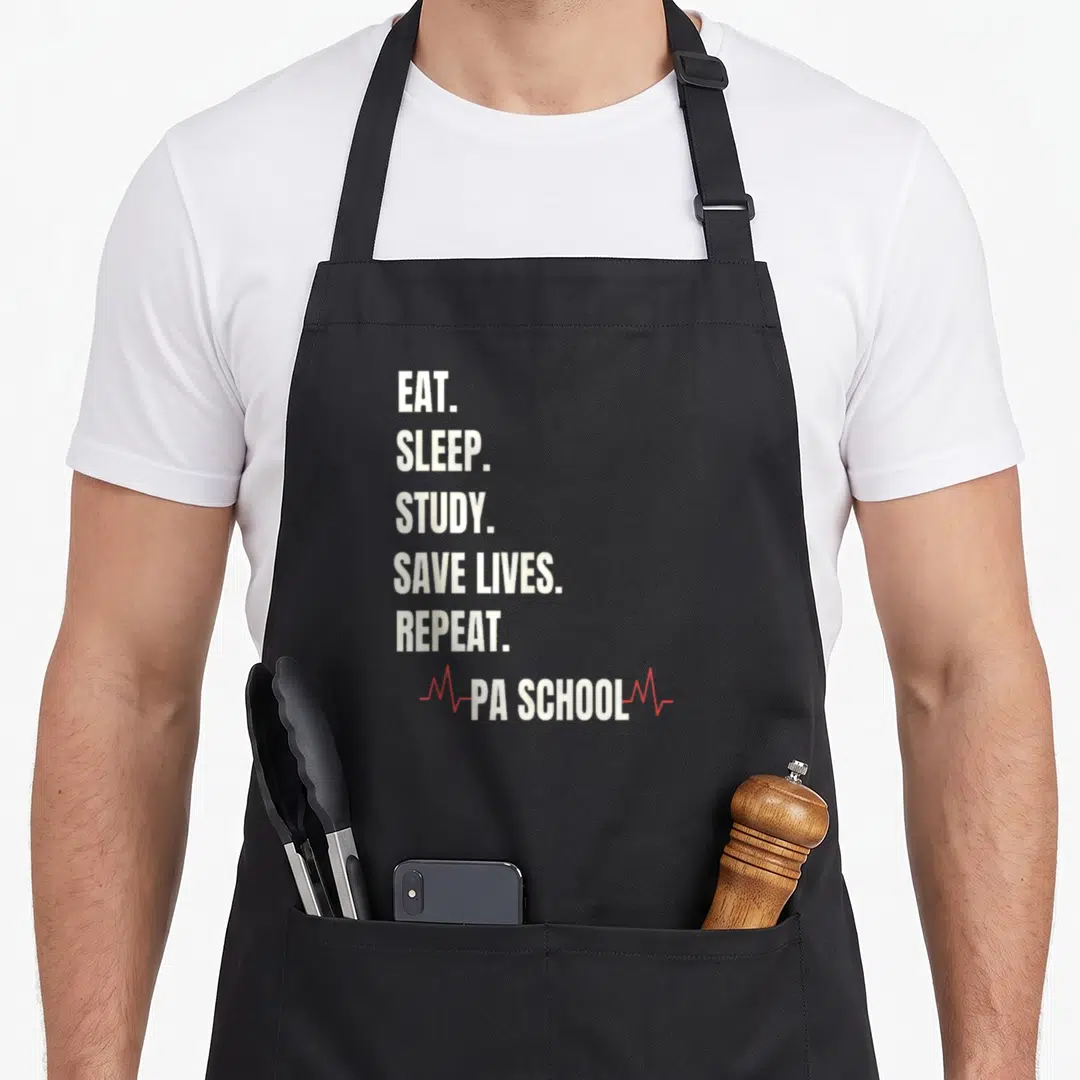 School physician apron - Stacked white text reading EAT SLEEP STUDY SAVE LIVES REPEAT PA SCHOOL with red heartbeat line — shown on a black cotton canvas apron against a white background