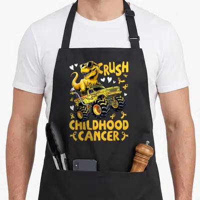 Childhood truck apron - Yellow T-Rex in sunglasses on monster truck with CRUSH CHILDHOOD CANCER text and yellow ribbons — shown on a black cotton canvas apron against a white background