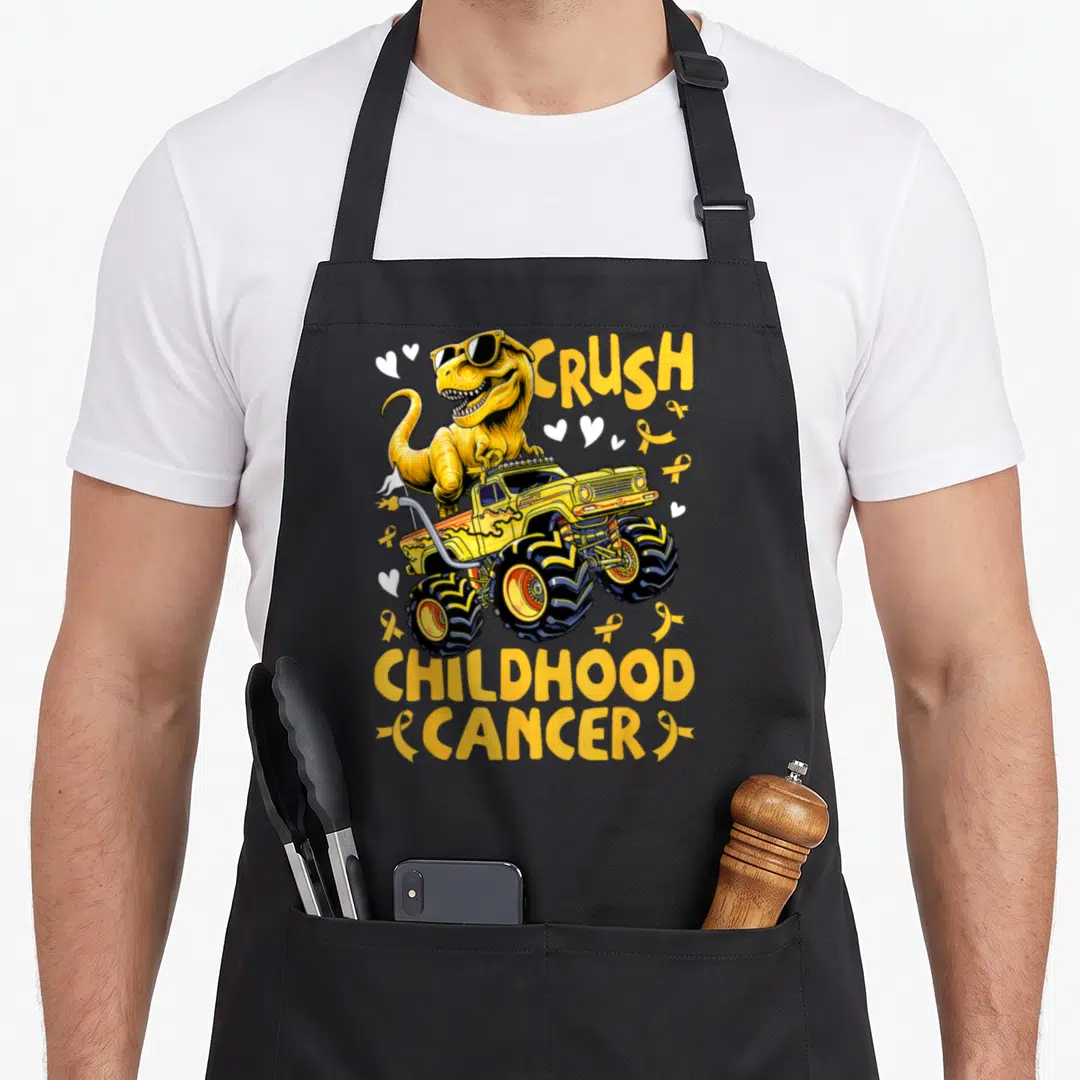 Childhood truck apron - Yellow T-Rex in sunglasses on monster truck with CRUSH CHILDHOOD CANCER text and yellow ribbons — shown on a black cotton canvas apron against a white background
