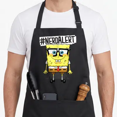 Squarepant nerd apron - #NERDALERT text above SpongeBob SquarePants wearing glasses and a red tie — shown on a black cotton canvas apron against a white background