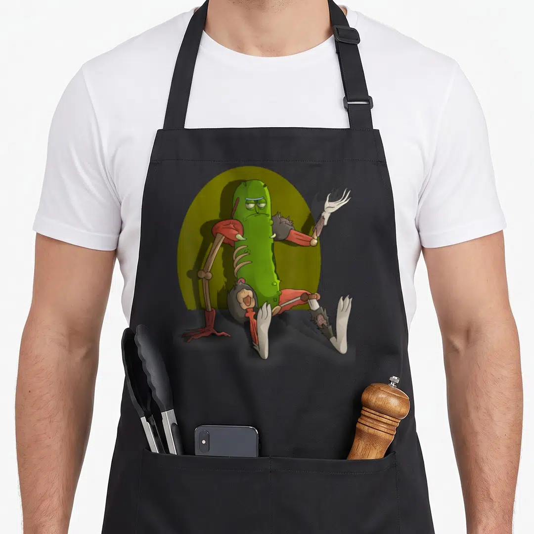 Interview pickle apron - Pickle character fused with bones and flesh against olive oval background — shown on a black cotton canvas apron against a white background