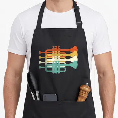Trumpet marching band apron - Four stacked trumpets in orange, yellow, off-white, and teal with distressed retro texture — shown on a black cotton canvas apron against a white background