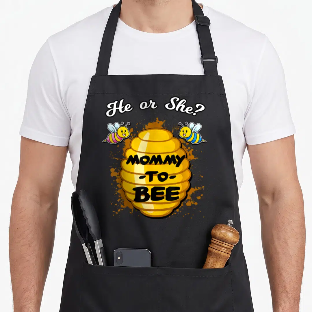 Baby bee apron - Yellow beehive with He or She? MOMMY -TO- BEE text and two bees — shown on a black cotton canvas apron against a white background