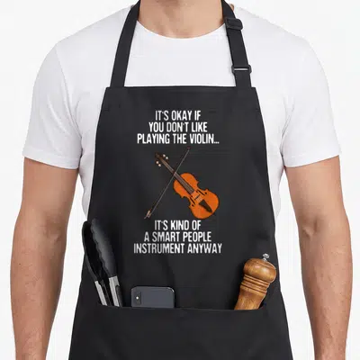 Instrument violin apron - Orange violin and bow crossed in X shape with white sarcastic text blocks above and below — shown on a black cotton canvas apron against a white background