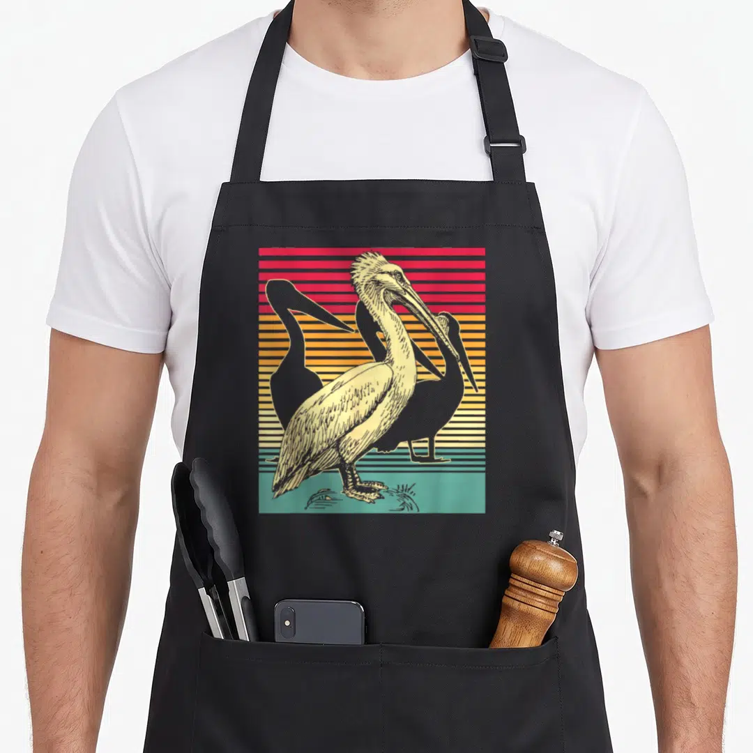 Pelican groomer apron - Retro pelican illustration on red orange yellow and green horizontal stripes — shown on a black cotton canvas apron against a white background