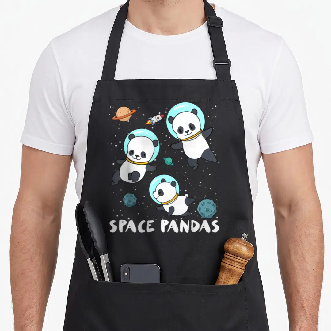 Space travel aprons - Three cartoon pandas in blue helmets floating near planets and rockets with white text below — shown on a black cotton canvas apron against a white background