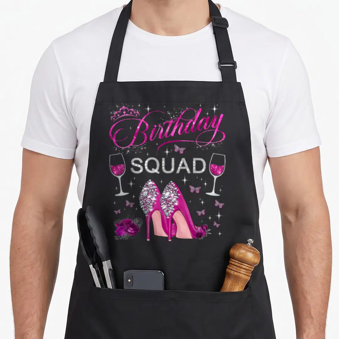 Heel butterfly apron - Birthday Squad text with high heels, wine glasses, butterflies and roses in pink and silver — shown on a black cotton canvas apron against a white background