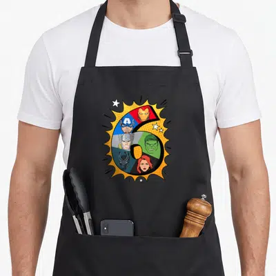 Heroe 6th birthday apron - Number 6 divided into sections with character heads on yellow burst with white stars — shown on a black cotton canvas apron against a white background