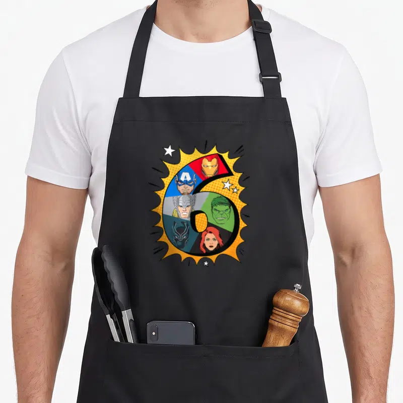 Heroe 6th birthday apron - Number 6 divided into sections with character heads on yellow burst with white stars — shown on a black cotton canvas apron against a white background