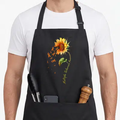 Multiple sunflower apron - Watercolor sunflower with orange ribbons and curved text reading Multiple Sclerosis Awareness — shown on a black cotton canvas apron against a white background