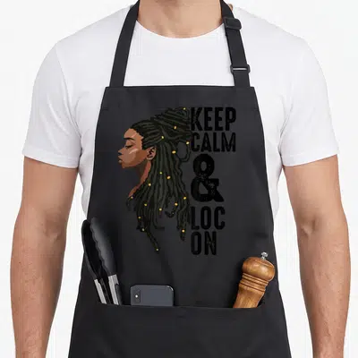 Melanin kwanzaa apron - Cartoon woman profile with locs and stacked text Keep Calm Loc — shown on a black cotton canvas apron against a white background