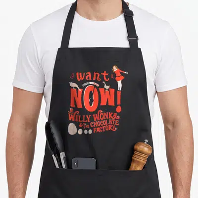 Willy wonka factory aprons - Veruca Salt stands on I Want It Now text with birds and candy eggs in red white beige — shown on a black cotton canvas apron against a white background