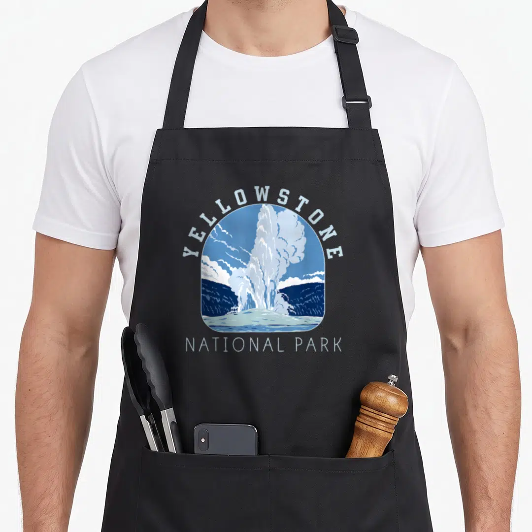 Faithful national apron - Blue and white geyser illustration in a rounded frame with arched text — shown on a black cotton canvas apron against a white background