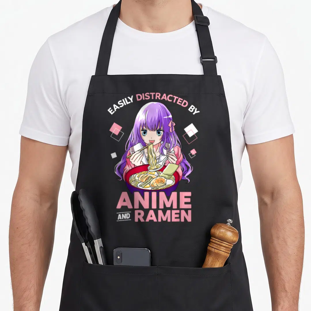 Distracted ramen anime apron - Purple haired anime girl eating ramen with pink and white text arching overhead — shown on a black cotton canvas apron against a white background