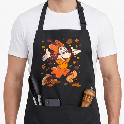 Strolling fall aprons - Cartoon mouse in orange dress surrounded by scattered brown and yellow autumn leaves and acorns — shown on a black cotton canvas apron against a white background