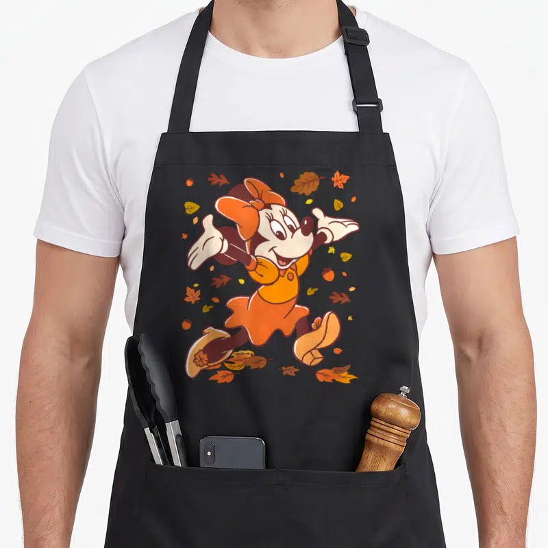 Strolling fall aprons - Cartoon mouse in orange dress surrounded by scattered brown and yellow autumn leaves and acorns — shown on a black cotton canvas apron against a white background