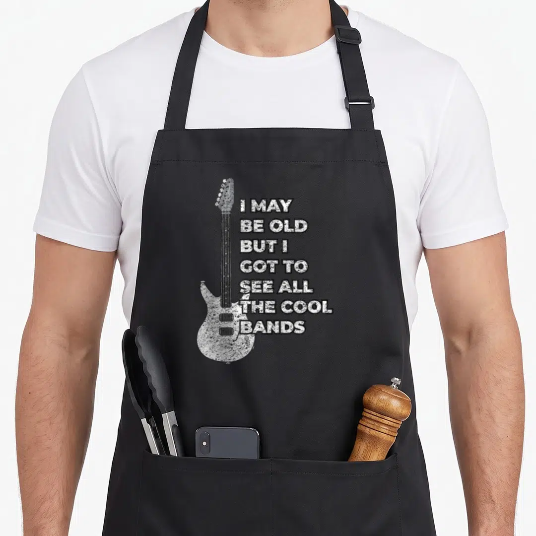 Vintage rock 80s apron - Distressed white electric guitar next to seven lines of stacked black text on a dark background — shown on a black cotton canvas apron against a white background