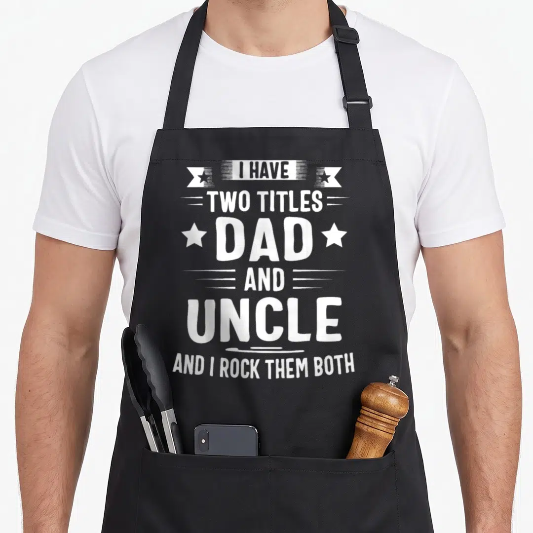 Uncle titles dad apron - White stacked text reading I Have Two Titles Dad and Uncle and I Rock Them Both with stars — shown on a black cotton canvas apron against a white background