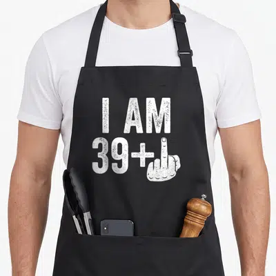 Middle finger 40th birthday apron - White distressed text I AM 39+ next to an extended middle finger hand — shown on a black cotton canvas apron against a white background