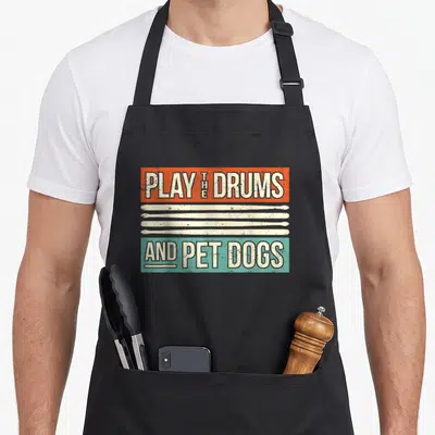 Drummer custom pet apron - Retro orange and teal blocks with three white drumsticks and text about drums and dogs — shown on a black cotton canvas apron against a white background
