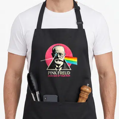 Dark joke apron - Sigmund Freud portrait in triangle with rainbow prism and Pink Freud text — shown on a black cotton canvas apron against a white background