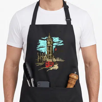 London travel aprons - Big Ben line art with red bus, car, heart, and London text — shown on a black cotton canvas apron against a white background