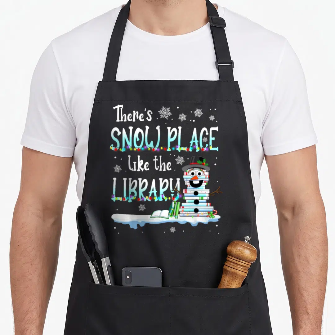 Librarian christmas apron - Stacked text ‘There’s SNOW PLACE like the LIBRARY’ beside book snowman with lights — shown on a black cotton canvas apron against a white background