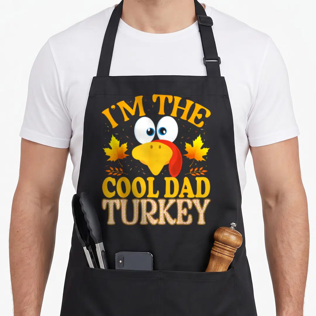 Animal thanksgiving apron - Cartoon turkey head with I'm The Cool Dad text and floral pattern letters — shown on a black cotton canvas apron against a white background