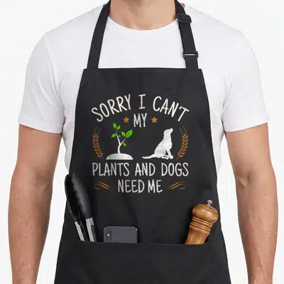 Dog gardener apron - Text Sorry I Can't My Plants and Dogs Need Me with dog and plant silhouette — shown on a black cotton canvas apron against a white background