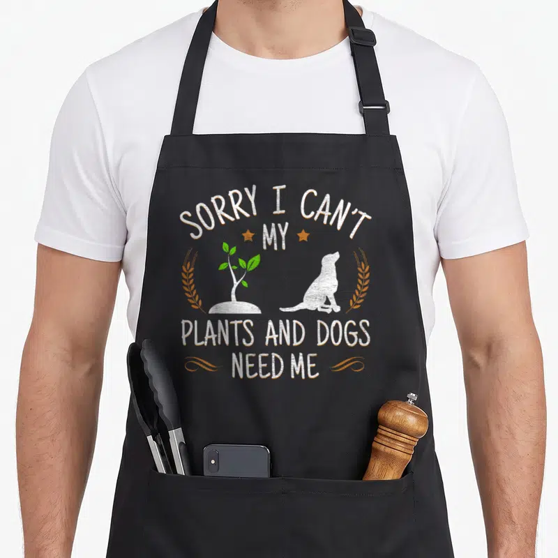 Dog gardener apron - Text Sorry I Can't My Plants and Dogs Need Me with dog and plant silhouette — shown on a black cotton canvas apron against a white background