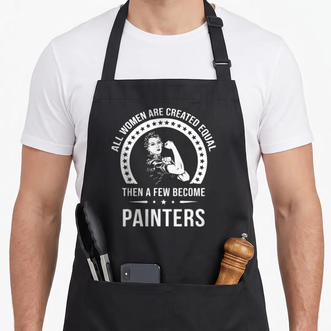 Funny painter apron - Retro woman flexing arm in star circle with white text about women becoming painters — shown on a black cotton canvas apron against a white background