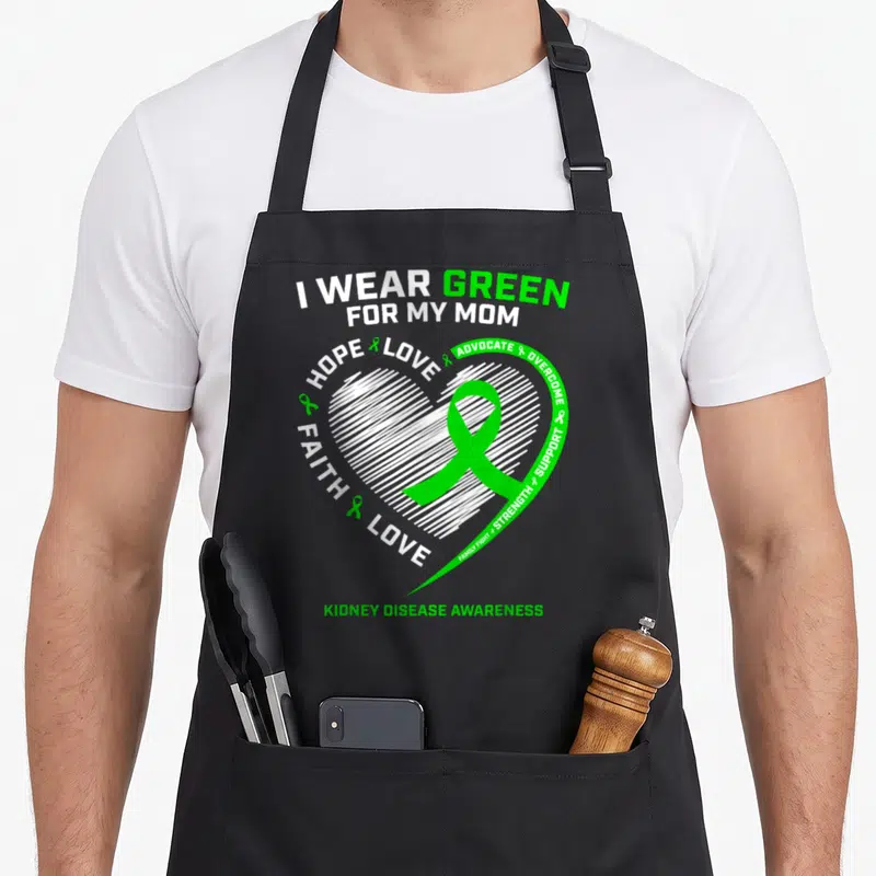 Fighter kidney disease awareness apron - Green ribbon inside white lined heart surrounded by advocacy text I wear green — shown on a black cotton canvas apron against a white background