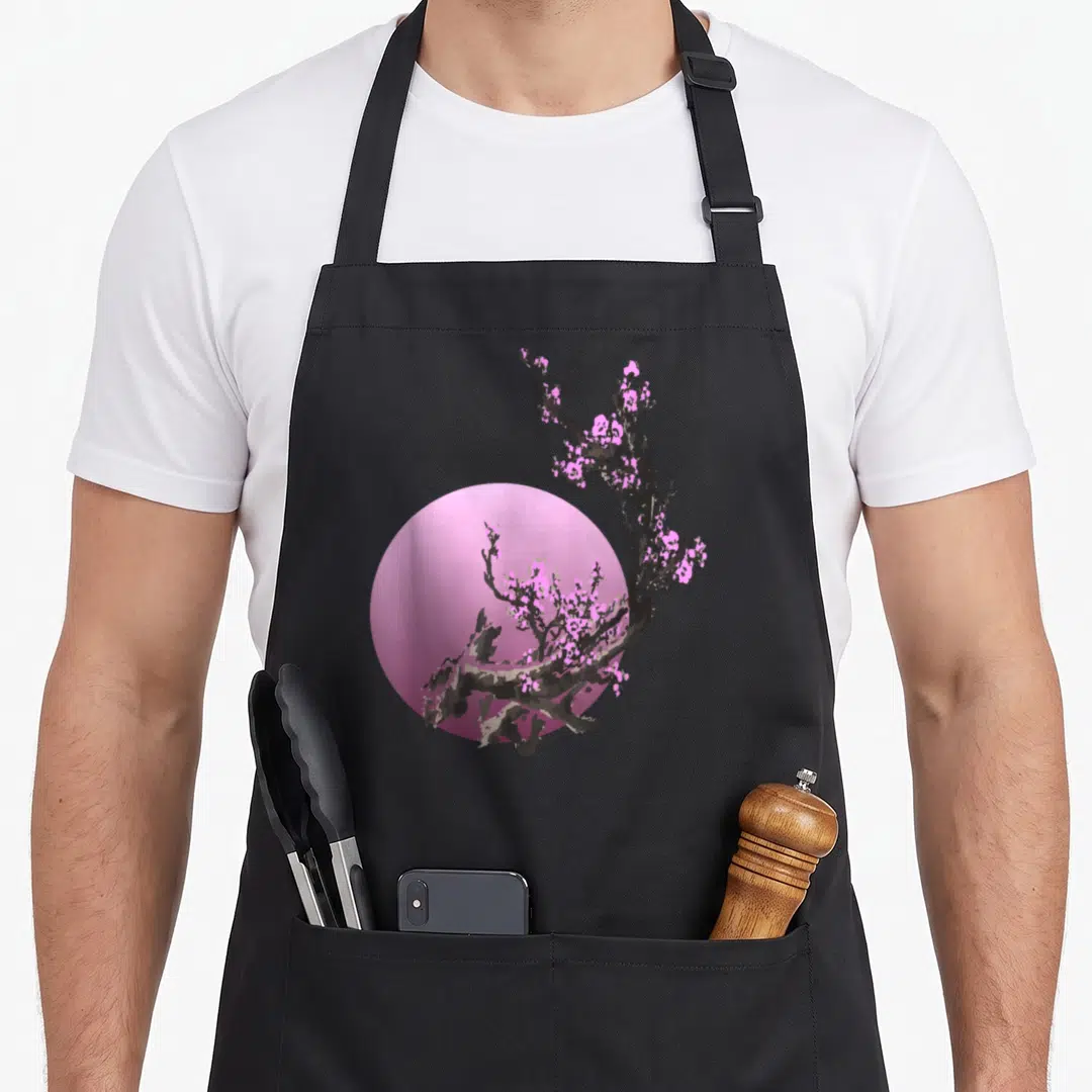 Rosa cherry print apron - Grey branch with pink blossoms overlapping a large pink circle on a grey background — shown on a black cotton canvas apron against a white background