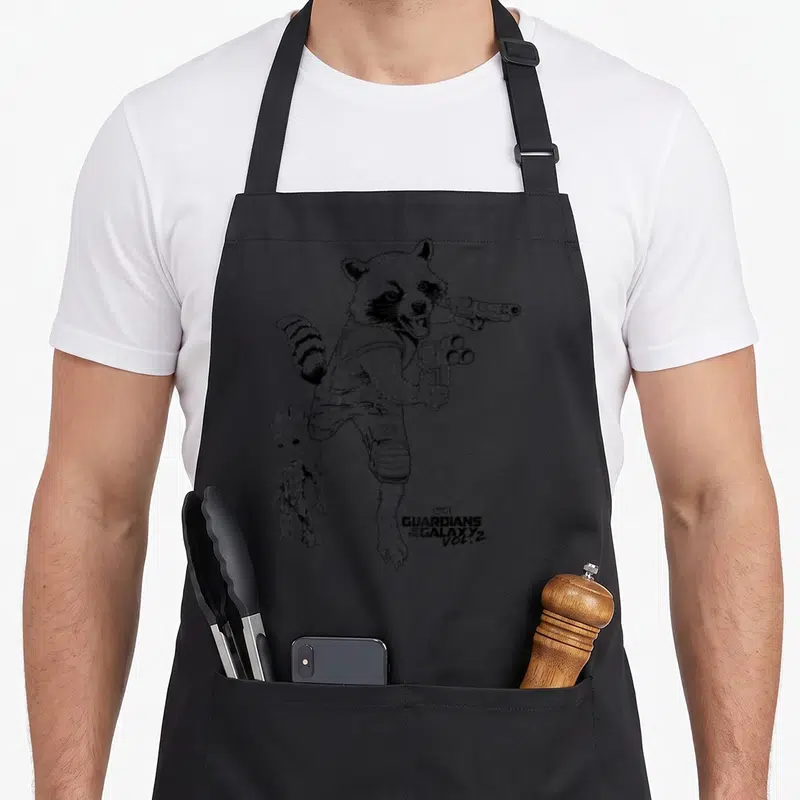 Guardian milky way apron - Line art of Rocket Raccoon holding two guns with Groot and movie title text — shown on a black cotton canvas apron against a white background