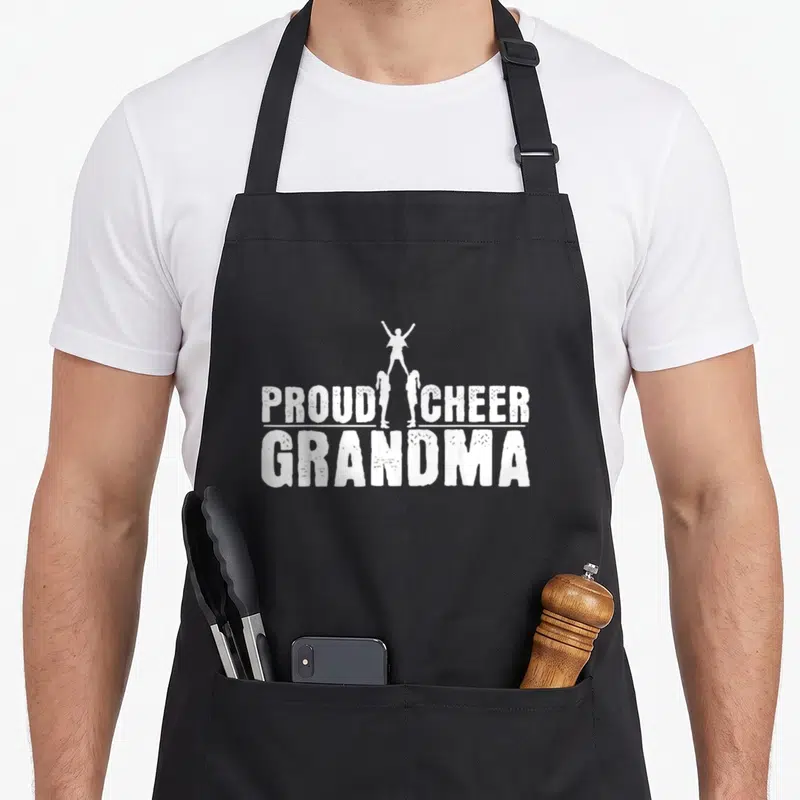 Cheerleader grandma apron - White PROUD CHEER GRANDMA text with three cheerleader silhouettes in a stunt — shown on a black cotton canvas apron against a white background