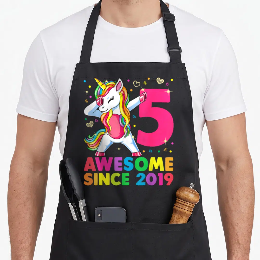 Dabbing 5th birthday apron - Cartoon unicorn dabbing next to pink number 5 with rainbow text Awesome Since 2019 — shown on a black cotton canvas apron against a white background