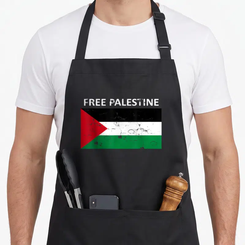Fist palestine apron - Distressed flag with black white green red stripes and free palestine text — shown on a black cotton canvas apron against a white background