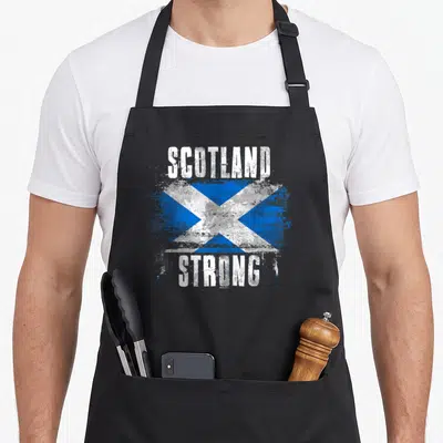 Scotland strong pride apron - Distressed blue white saltire flag with SCOTLAND STRONG text — shown on a black cotton canvas apron against a white background