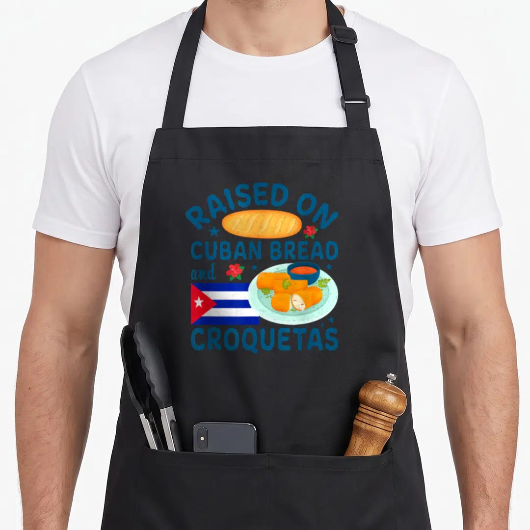 Cuban bread apron - Raised On Cuban Bread and Croquetas text with loaf, plate, and flag in blue orange red white — shown on a black cotton canvas apron against a white background