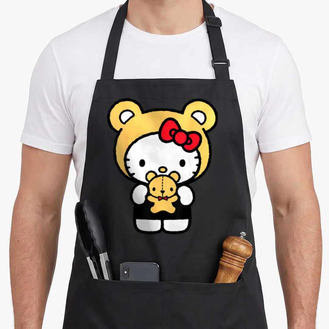 Dress teddy bear apron - Hello Kitty wearing yellow bear hood holding small teddy bear red bow — shown on a black cotton canvas apron against a white background