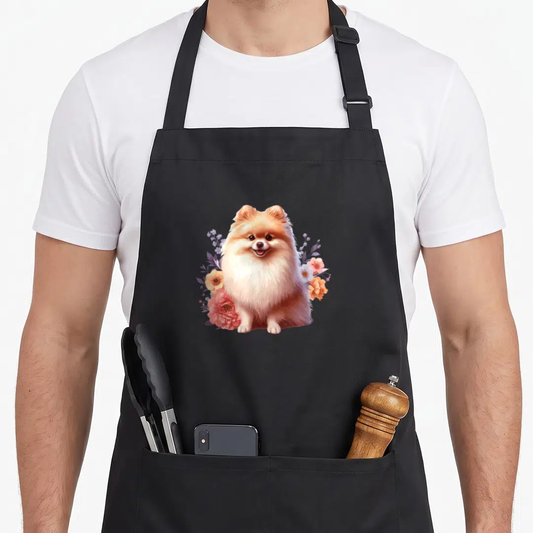 Pomeranian floral apron - Realistic fluffy Pomeranian dog centered among pink, orange, and white flowers and purple — shown on a black cotton canvas apron against a white background