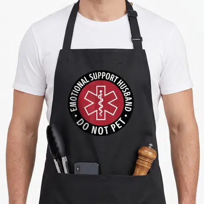 Support pet husband apron - Red circle with white Star of Life and rod, black border with white text reading emotional — shown on a black cotton canvas apron against a white background