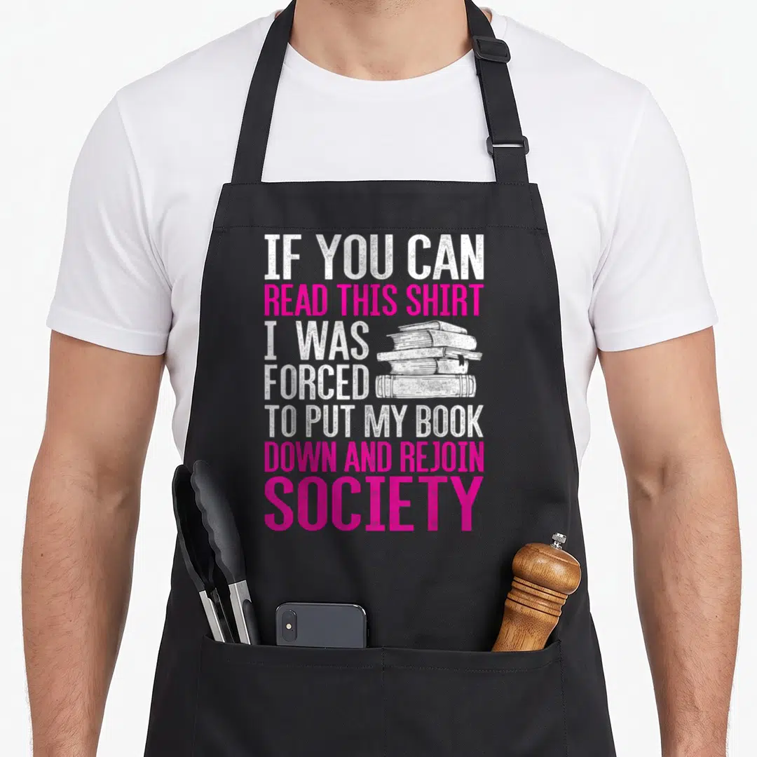 Forced reading book apron - Stacked white books next to pink and white distressed text about being forced to read — shown on a black cotton canvas apron against a white background