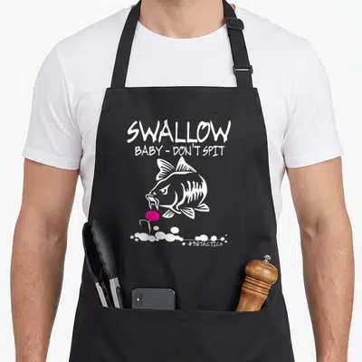 Swallow fishing aprons - White cartoon fish facing pink lure below Swallow Baby Don Spit text — shown on a black cotton canvas apron against a white background
