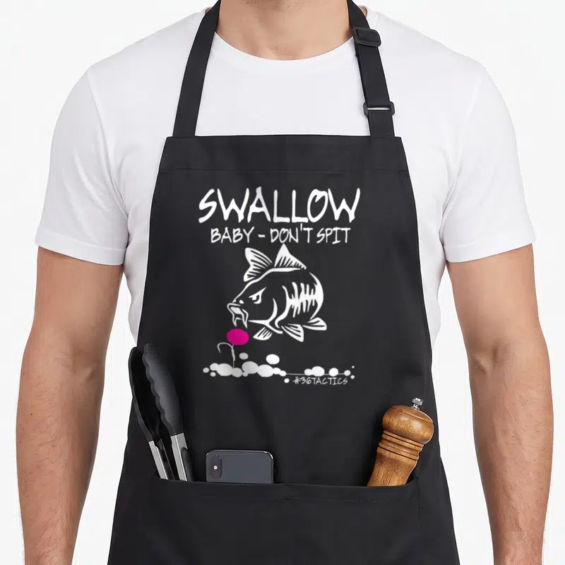 Swallow fishing aprons - White cartoon fish facing pink lure below Swallow Baby Don Spit text — shown on a black cotton canvas apron against a white background
