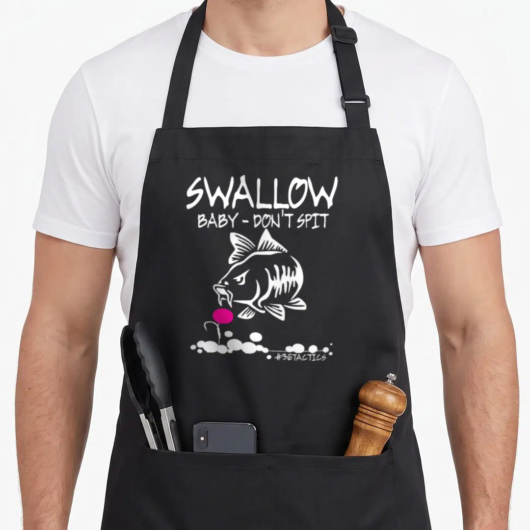 Swallow fishing aprons - White cartoon fish facing pink lure below Swallow Baby Don Spit text — shown on a black cotton canvas apron against a white background