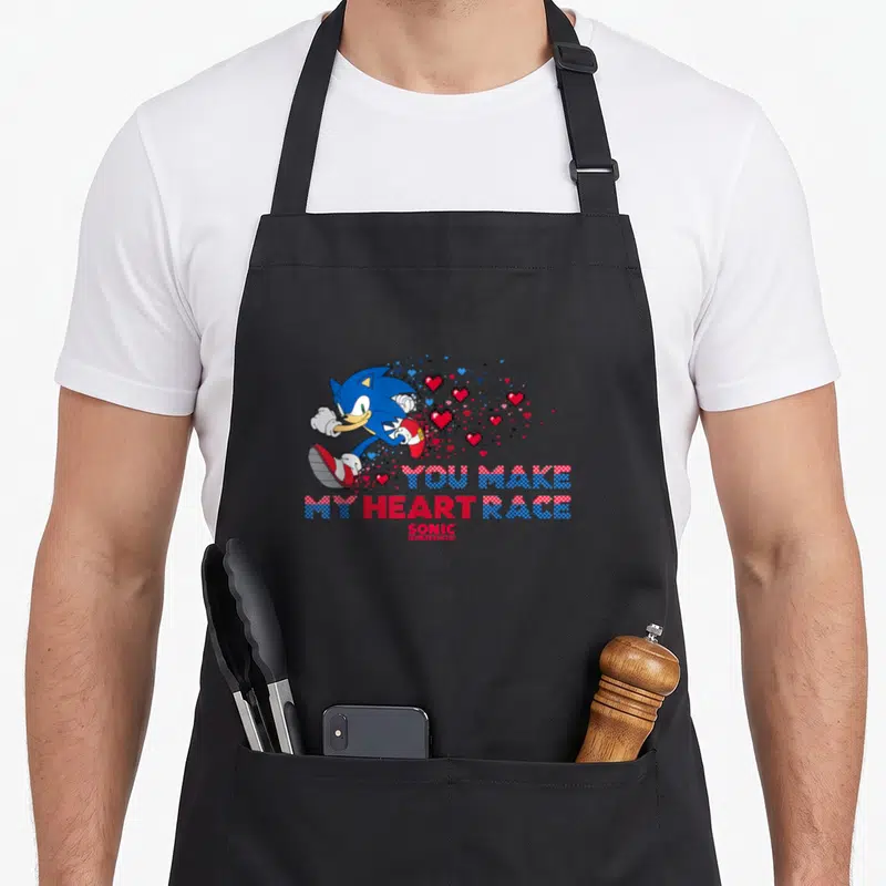 Race valentine's day apron - Sonic running left with pixel heart trail and YOU MAKE MY HEART RACE text — shown on a black cotton canvas apron against a white background