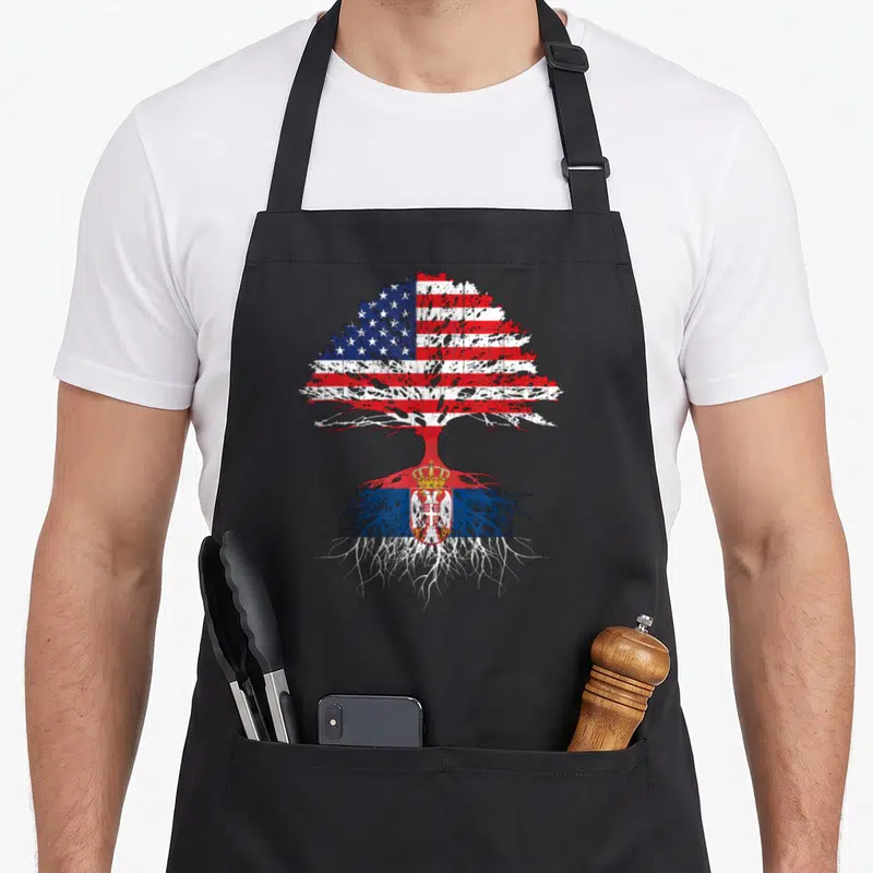 Serbia american flag apron - Distressed tree with USA flag leaves and Serbian flag roots on canvas — shown on a black cotton canvas apron against a white background