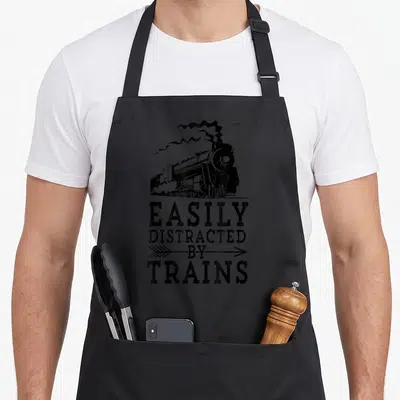 Easily steam locomotive apron - Black distressed steam locomotive with smoke and stacked text EASILY DISTRACTED — shown on a black cotton canvas apron against a white background