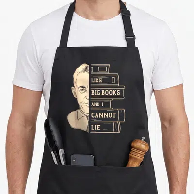 Book big w aprons - Tan man portrait next to stacked books with I like big books cannot lie text — shown on a black cotton canvas apron against a white background